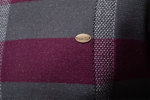 Détail macro du pull en maille rayé gris foncé et bordeaux pour homme avec logo métal