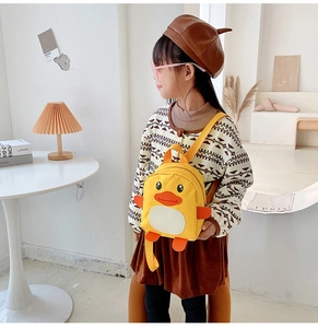 Side view of cute yellow duck backpack on toddler girl in a cozy indoor setting
