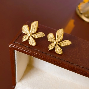 Macro shot of gold floral earrings with textured detail on a premium leather jewelry box