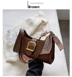 Detail of coffee brown crocodile pattern baguette bag with gold buckle and silk scarf strap