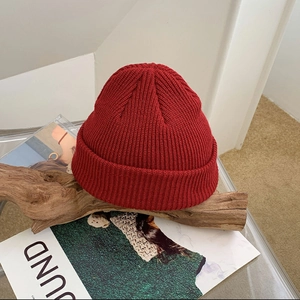Detail of red chunky knit beanie hat with cuffed design on wooden log and magazine