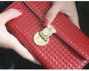 Détail d'une pochette en cuir verni rouge avec texture géométrique et fermoir doré