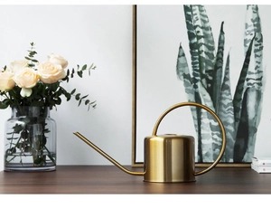 Golden stainless steel watering can with long spout on a wooden table with flowers