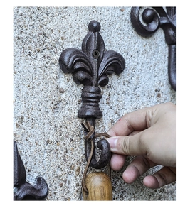 Detail of hand tying a rope to a vintage fleur-de-lis cast iron wall hook on concrete wall