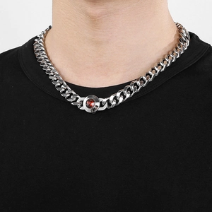 Detail of silver Cuban chain featuring a red gemstone pendant and crystal clasp on neck