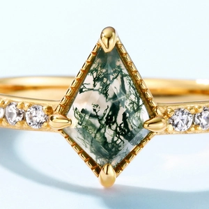 Kite-cut green moss agate ring in gold setting with side accents on light blue background