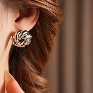 Close-up of polished silver metal knot stud earrings worn by a model for a stylish look