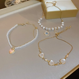 Close-up of gold-plated bracelets featuring opal heart charms and elegant pearls
