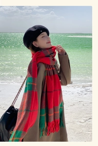 Detail of red and green plaid scarf with tassels on a soft winter knitted fabric