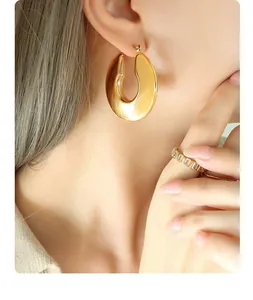 Detailed view of large gold U-shaped titanium earrings and zircon ring on female model