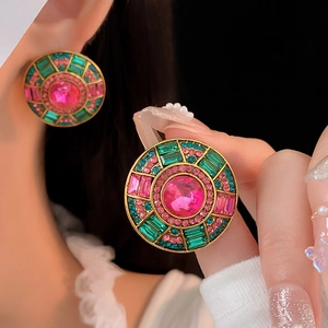 Dettaglio di orecchini vintage dorati con pietre rosa e cristalli verdi brillanti