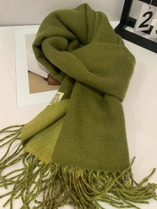 Detailed view of a soft green winter scarf featuring tassel trim and a woven tag
