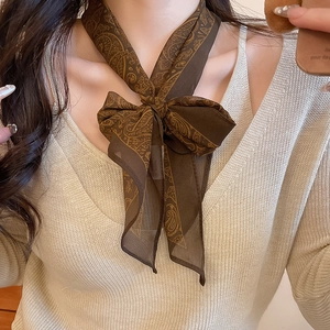 Close-up of a brown paisley chiffon scarf tied as a bow necklace on a beige sweater