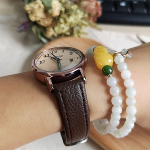 Detailed view of rose gold quartz watch with brown leather strap and beaded charm bracelet