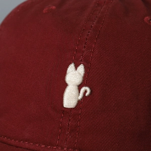 Makro-Detail der weißen Katzenstickerei auf weinrotem Twill-Baumwollstoff der Kappe