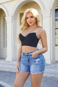 Outdoor lifestyle shot of blue distressed denim shorts with ripped details and raw hem