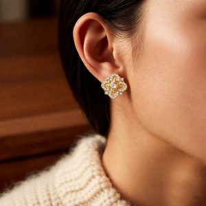 Close-up of gold-plated flower earring with zircon on a model wearing a knit sweater