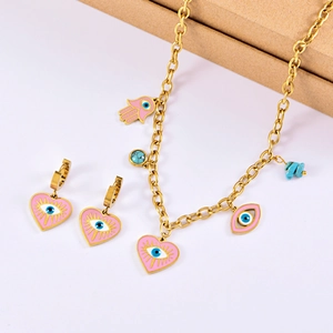 Detail of pink enamel heart and evil eye charms on golden stainless steel jewelry set