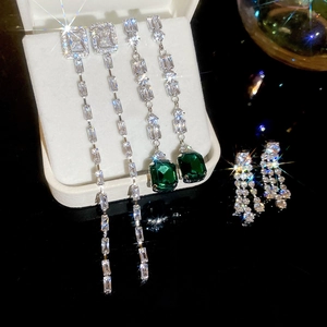 Close-up of silver tassel earrings with green rectangular gems and sparkling zircons