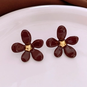 Détail de boucles d'oreilles fleurs en acrylique rouge foncé avec centre doré sur plat