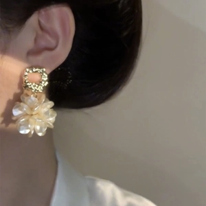 Detail of floral earring on model featuring gold texture ring and pearly petals