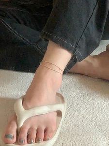 Close-up of a double-layered golden snake chain anklet with beads on a model wearing flip-flops