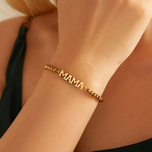 Detailed close-up of 18K gold beaded bracelet with MAMA letter charm on wrist