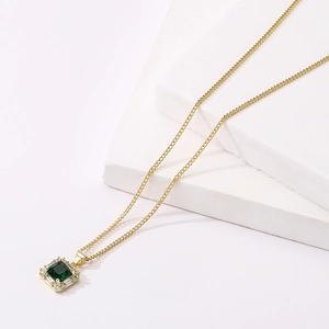 Close-up of 18K gold-plated necklace with a square emerald pendant on white stone