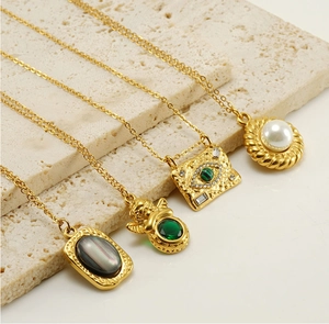Close-up of four gold necklaces with green stone, pearl, and evil eye on beige stone