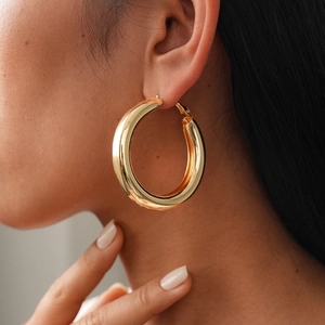 Close-up of a model wearing chunky gold hoop earrings with a polished metallic finish