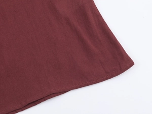 Dettaglio dell'orlo di una camicia rosso vino con cuciture precise e trama in lino