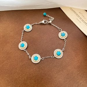 Detail of bohemian gold-rimmed turquoise beads on a silver chain bracelet with vintage lace