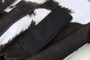 Detail view of cow print jacket fabric with a stitched black faux leather patch