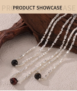 Detail view of steel bead chain necklaces with tiger eye stone pendant on stone and wood