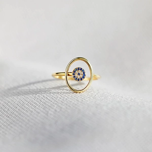 Minimalist gold S925 silver ring featuring a blue evil eye pave charm on a grey fabric