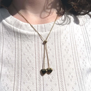 Detail of gold Y-chain necklace with heart pendants on a white textured blouse