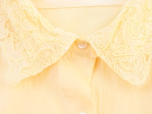 Détail du col d'une chemise jaune pâle avec broderie en dentelle complexe et bouton