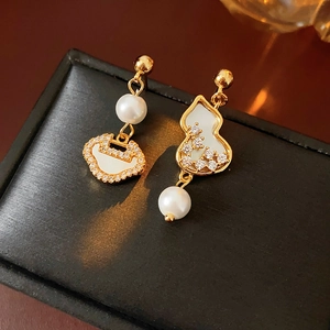 Detailed close-up of gold-plated gourd and lock earrings with pearls on black leather