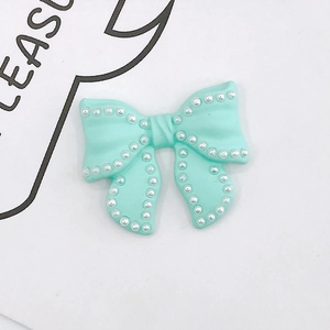 Macro detail of mint green resin bow accessory with white pearl trim and center texture