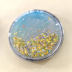 Detail of round folding makeup mirror with blue quicksand and star sequins in silver frame