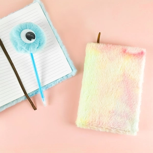 Dettaglio del taccuino di peluche arcobaleno con penna soffice su sfondo rosa