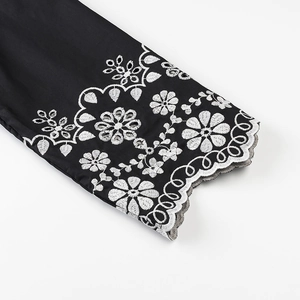 Detailed close-up of intricate white floral embroidery on a black sleeve with scalloped edge