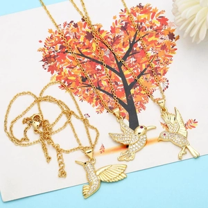 Detail view of dainty gold hummingbird necklaces with crystal pavé on artistic card