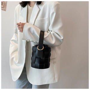 Detail of black woven leather bucket bag with gold handle held by model in white blazer