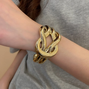 Close-up of golden chunky twisted knot cuff bracelet on wrist over a grey garment