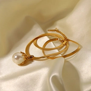 Detailed view of a gold snake chain necklace with a large white pearl on silk fabric