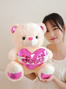 Detail of a beige teddy bear with a pink metallic LOVE heart held by a model
