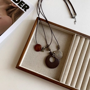 Detail of a minimalist leather cord necklace featuring round wood and spiral metal charms