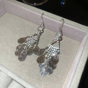Close-up of sparkling leaf fringe earrings with rhinestones on gray velvet background
