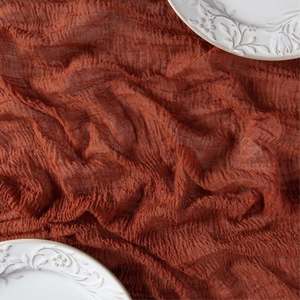 Detailed texture of rust-red boho cheesecloth table runner with natural wrinkles